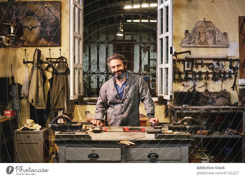 Frontansicht eines glücklichen Handwerkers im Atelier stehend Kunsthandwerker Glück Sauberkeit Gravur Gewebe golden Rahmen Kunstgewerbler Kleinunternehmen
