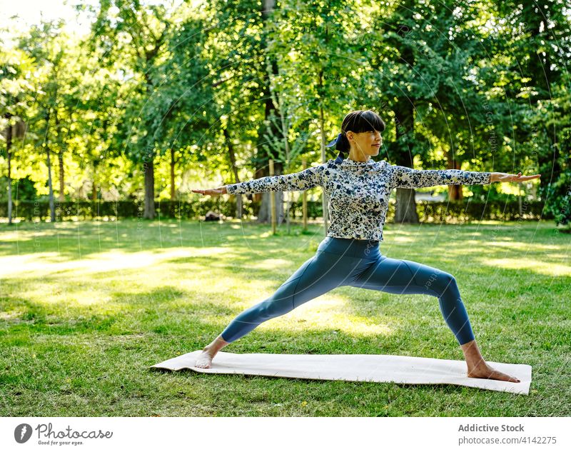 Zufriedene Frau beim Yoga in Virabhadrasana im Park Krieger-Pose üben beweglich sich[Akk] entspannen virabhadrasana Unterlage Barfuß Sportbekleidung Übung
