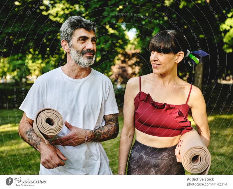 Fröhliches Paar mit Yoga-Matten zu Fuß im Park Unterlage Spaziergang heiter Zusammensein positiv reden Glück Kommunizieren Gespräch üben Wellness Aktivität