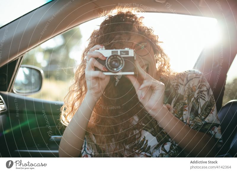 Glückliche Frau, die ein Foto mit der Kamera aus dem Auto heraus macht fotografieren Fotoapparat digital Moment PKW Augen geschlossen Sonnenschein heiter