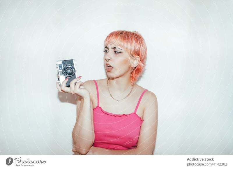 Rebellische Frau, die mit einer Retro-Kamera fotografiert tausendjährig auflehnen fotografieren retro Fotograf unanständig altehrwürdig Piercing rosa Haare Stil