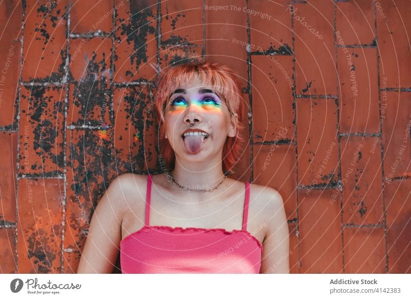 Ungezogene Frau mit herausgestreckter Zunge in der Stadt tausendjährig unanständig Zunge zeigen rosa Haare Gesicht machen sorgenfrei Regenbogen Verhalten