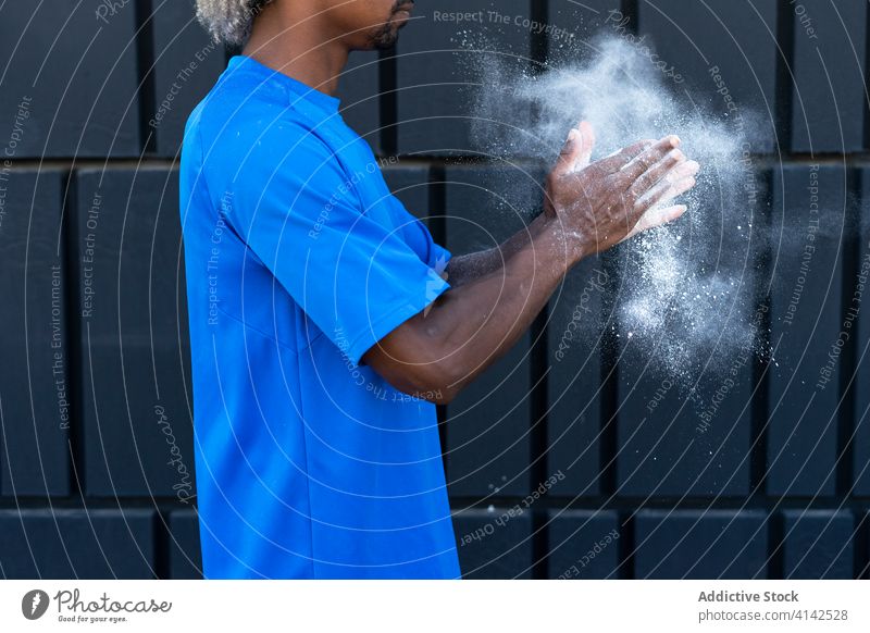 Anonymer schwarzer Sportler, der mit Pulver in die Hände klatscht Kreide in die Hände klatschen Training Wand modern vorbereiten Gebäude Athlet männlich Kraft