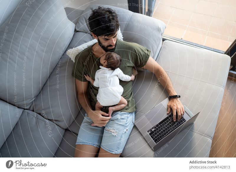 Beschäftigter Vater mit Kleinkind benutzt Laptop Baby Arbeit freiberuflich Sofa beschäftigt neugeboren Projekt benutzend männlich Vaterschaft Netbook heimwärts