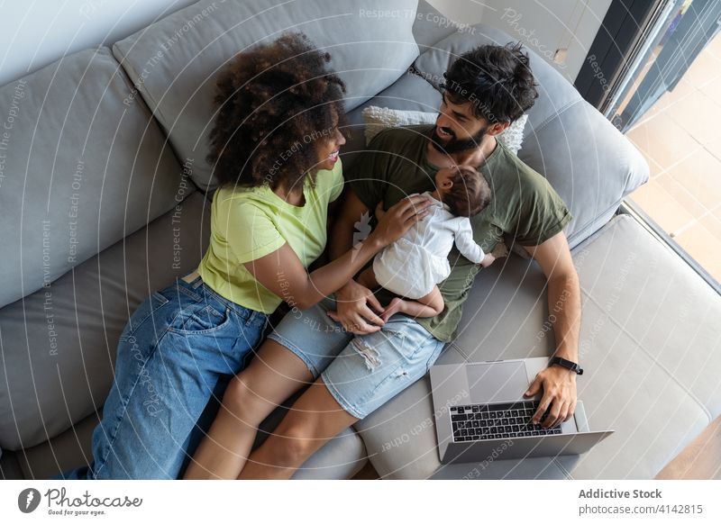 Fröhliche multiethnische Familie auf dem Sofa liegend Zusammensein Einheit Mutter neugeboren Paar Säugling Lügen Liege Vater heimwärts rassenübergreifend