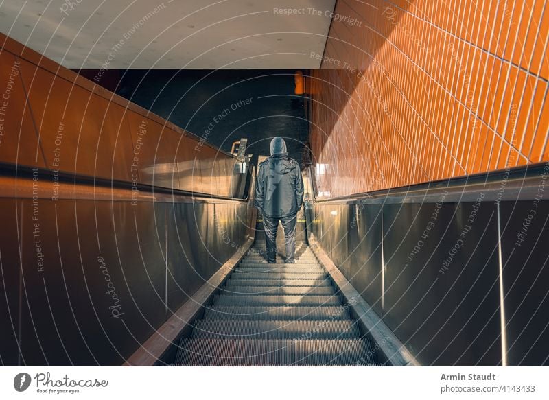 Berliner U-Bahn, Rückenansicht eines jungen Mannes auf einer Rolltreppe schwarz Bekleidung dunkel dreckig nach unten Europa Angst Gangsterin Deutschland schäbig