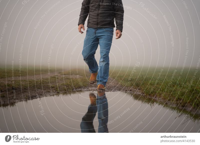 Junger Mann spaziert im Nebel in der Natur auf eine Wasserpfütze zu allein gehen mann natur outdoor spazieren spiegelung wandern wasser wiese Außenaufnahme