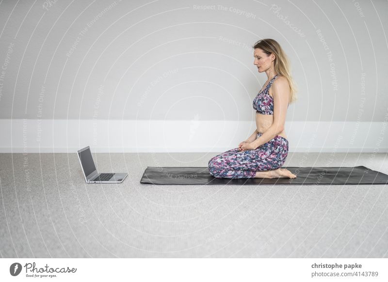Frau macht Yoga Zuhause mit Laptop zuhause online Notebook digital Lifestyle Sport sportlich entspannung entspannen Matte sitzen blond Computer Internet