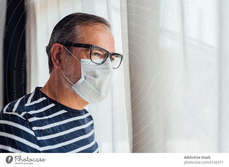 Bärtiger Mann mit Atemschutzmaske schaut aus dem Fenster Balkon Morgen heimwärts Appartement männlich Vollbart Lifestyle ruhig Gelassenheit friedlich