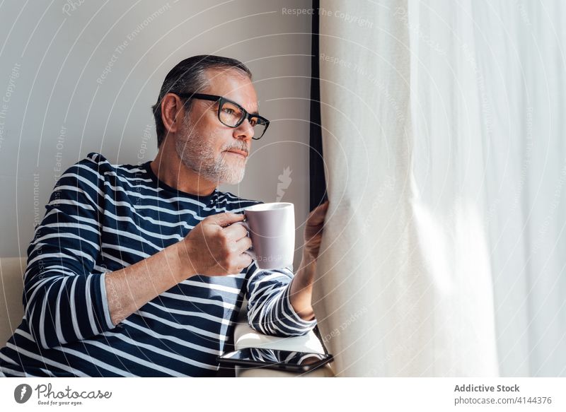 Bärtiger Mann mit Heißgetränk schaut aus dem Fenster trinken Balkon Morgen ruhen lässig heimwärts Appartement männlich Vollbart Lifestyle Getränk Kaffee Tee