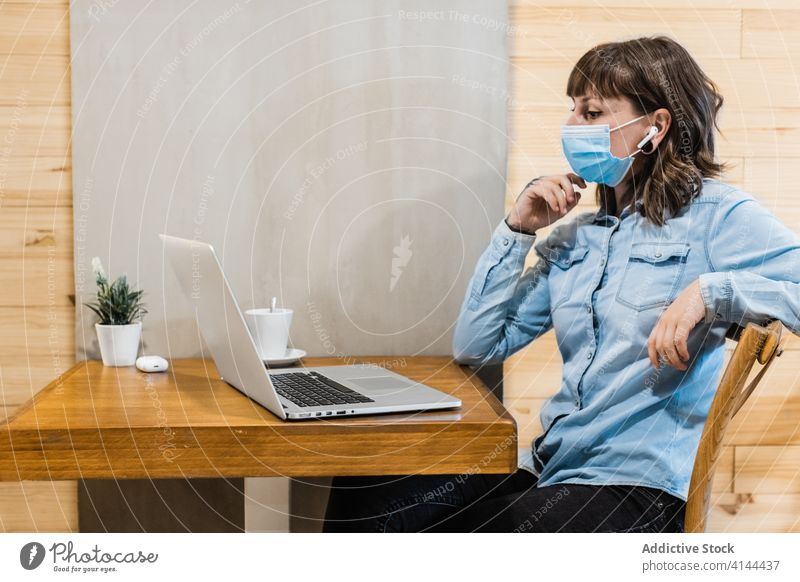 Konzentrierte Frau arbeitet in der Cafeteria mit Abstand am Laptop Arbeit freiberuflich Browsen Ohrstöpsel Fokus medizinisch Mundschutz Café Coronavirus
