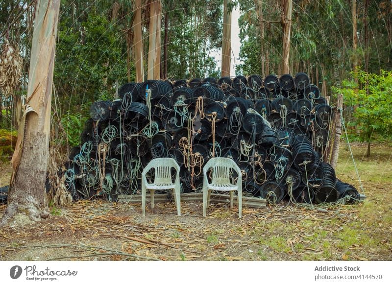 Stapel von Angelausrüstung und Stühlen in der Nähe wachsender Bäume Hocker Fischen Seil Gerät Haufen leer Baum Kofferraum Einsamkeit dreckig ruhig idyllisch