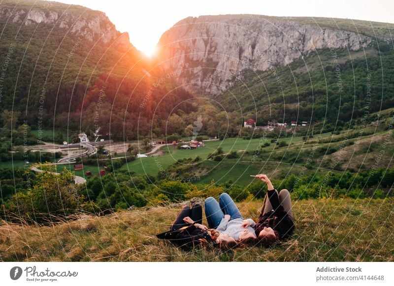 Freunde im Gras liegend in bergigem Gebiet Selfie Zusammensein Berge u. Gebirge sich[Akk] entspannen Sonnenuntergang Smartphone benutzend freundlich Unternehmen