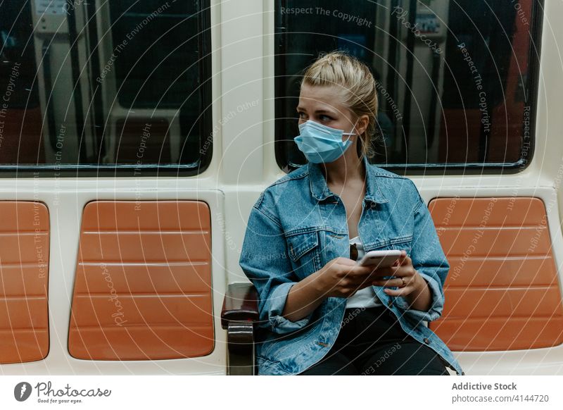 Junge Frau mit Schutzmaske benutzt Smartphone in der U-Bahn Coronavirus Passagier Mundschutz benutzend soziale Distanzierung COVID Pandemie Browsen