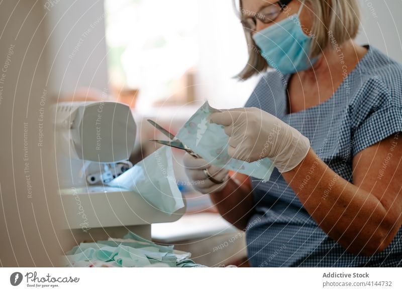 Näherin schneidet Stoff mit einer Schere zu Coronavirus Mundschutz nähen geschnitten Gewebe Frau Kunstgewerbler COVID handgefertigt Pandemie behüten