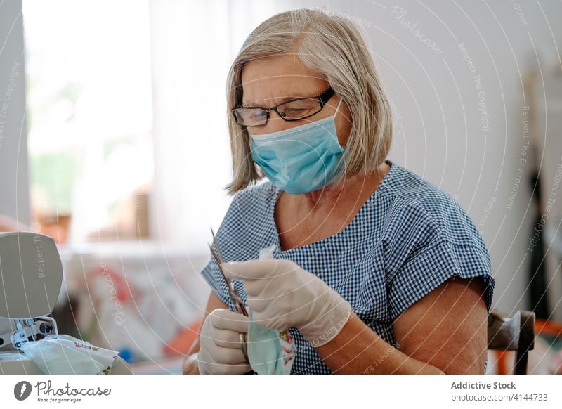 Näherin schneidet Stoff mit einer Schere zu Coronavirus Mundschutz nähen geschnitten Gewebe Frau Kunstgewerbler COVID handgefertigt Pandemie behüten