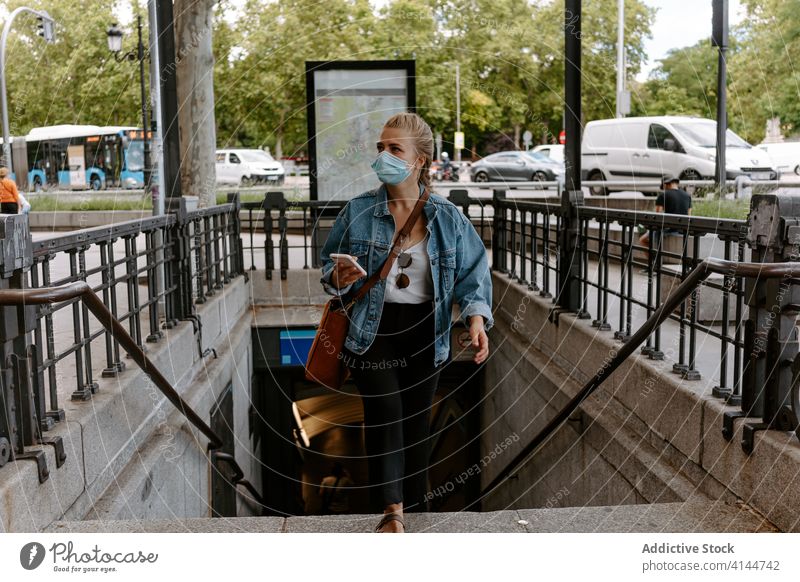 Junge Frau mit Maske und Smartphone geht eine Treppe hinauf auf die Straße Mundschutz Großstadt U-Bahn benutzend urban Coronavirus neue Normale Lifestyle
