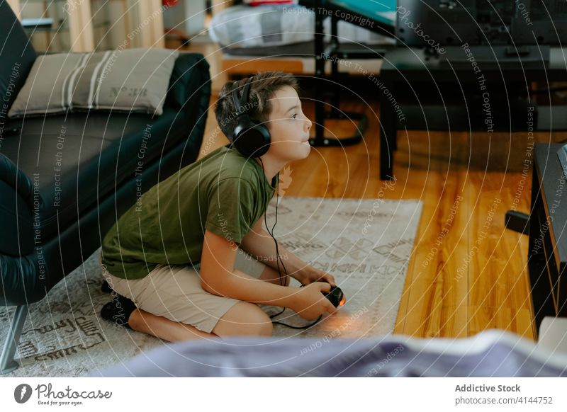 Konzentriertes Kind beim Videospiel auf der Couch Junge spielen Joystick Sofa Beine gekreuzt heimwärts unterhalten Gerät Apparatur Freizeit Konzentration wenig