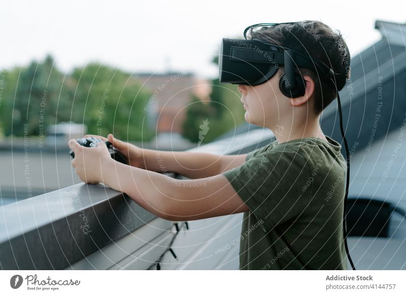 Konzentriertes Kind in VR-Headset auf Balkon Junge Schutzbrille benutzend Videospiel unterhalten Gerät Apparatur Innovation modern Erfahrung wenig T-Shirt
