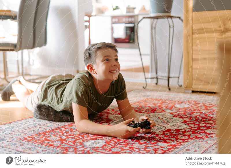 Niedliches Kind, das zu Hause auf dem Teppich liegt und an der Konsole spielt Junge Videospiel Lügen Stock spielen Joystick heimwärts Hobby Freizeit Gerät