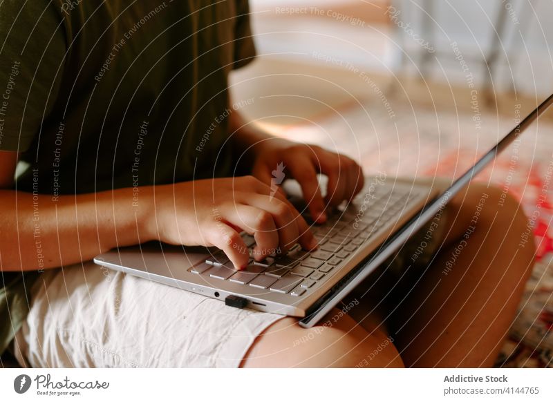 Fokussiertes Kind benutzt Laptop zu Hause Junge Tippen Stock heimwärts benutzend Internet Beine gekreuzt Gerät Apparatur Browsen online Anschluss wenig lässig