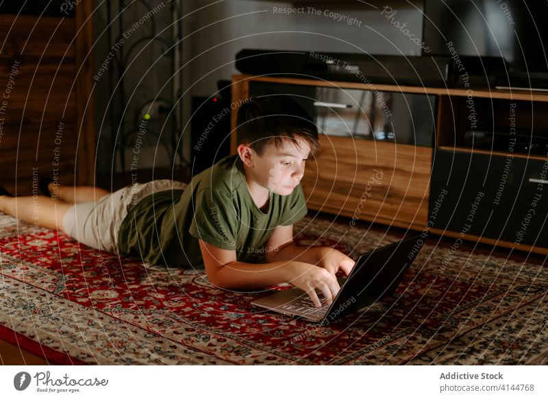 Nachdenkliches Kind sieht sich zu Hause einen Zeichentrickfilm auf dem Netbook an Junge zuschauen Laptop Lügen Stock besinnlich Film Gerät Internet Apparatur