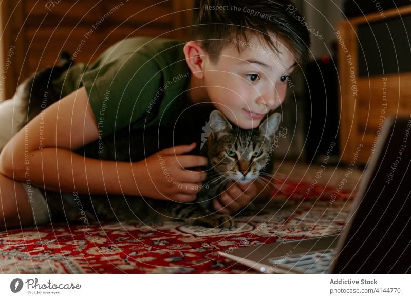 Kleiner Junge und Katze ruhen sich mit Laptop auf dem Boden aus Kind kuscheln Video Spaß haben heiter aufgeregt Glück Punkt Zusammensein bezaubernd zuschauen