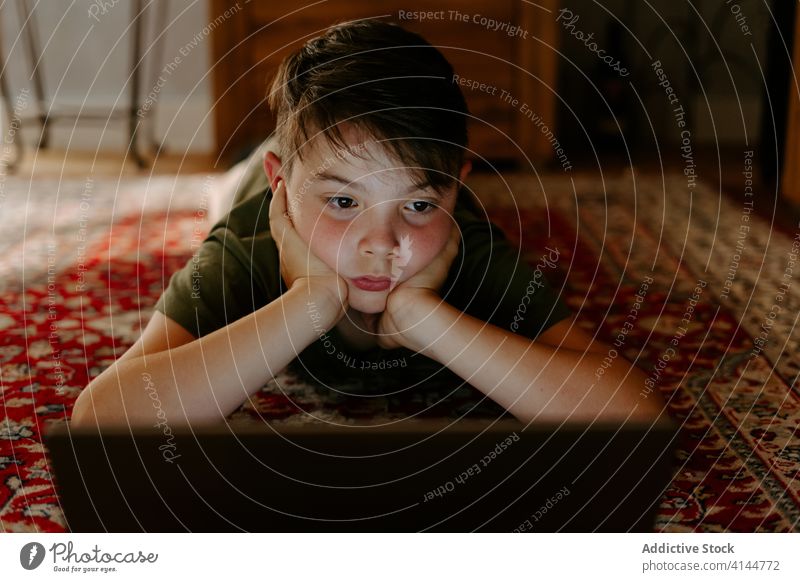 Nachdenkliches Kind sieht sich zu Hause einen Zeichentrickfilm auf dem Netbook an Junge zuschauen Laptop Lügen Stock Hand am Kinn besinnlich Film Gerät Internet