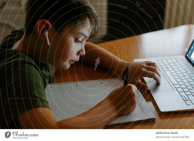 Konzentriertes Kind, das während des Online-Studiums zu Hause in ein Notizbuch schreibt Junge Hausaufgabe Anweisung Laptop schreiben Information Entfernung