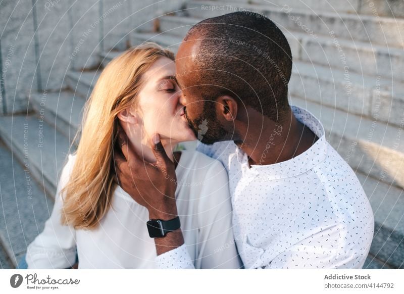 Glückliches, verschiedenartiges Paar küsst sich auf der Straße Kuss Bonden romantisch positiv Partnerschaft Liebe Zuneigung Umarmen modern lässig urban