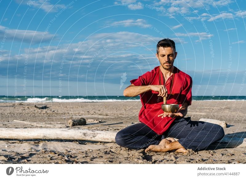 Ruhiger Mann entspannt sich beim Spielen einer Klangschale am Strand spielen tibetisch meditieren sich[Akk] entspannen halber Lotus Meer friedlich Asana