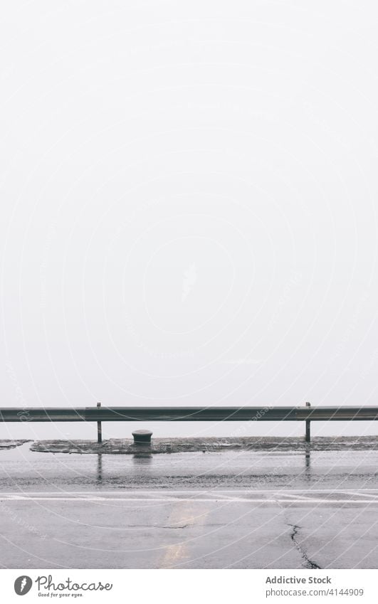 Nasse Asphaltstraße in einer nebligen Stadt nass Straße Nebel Morgen Großstadt leer Fahrbahn trist Metall Zaun verwittert Dunst Wetter erstaunlich ruhig