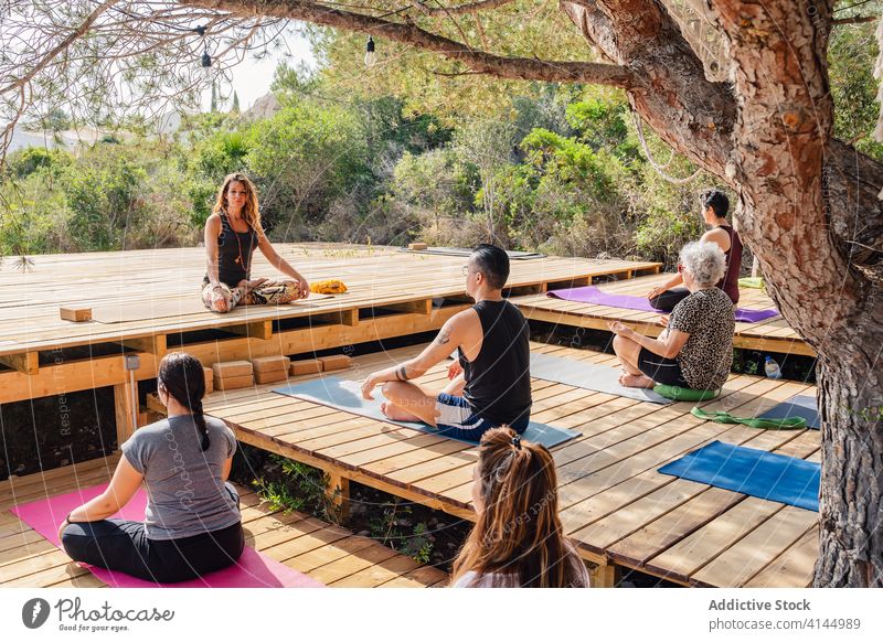 Gruppe von Menschen, die während einer Yogastunde mit einem Lehrer in der Lotus-Pose sitzen padmasana Garten Wellness Harmonie üben Zusammensein Vitalität