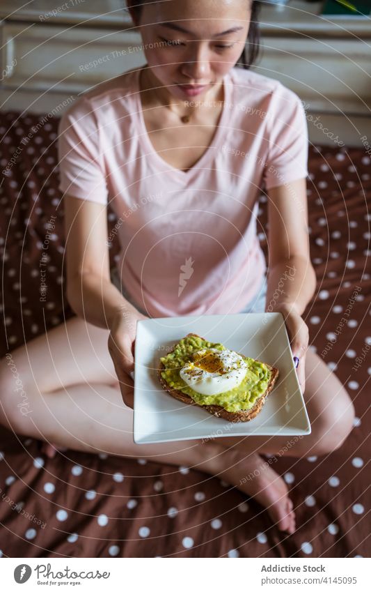 Asiatische Frau mit leckerem Frühstück auf dem Bett Avocado Zuprosten Ei natürlich Diät Gesundheit Morgen ethnisch asiatisch Pyjama weich Teller frisch Mahlzeit