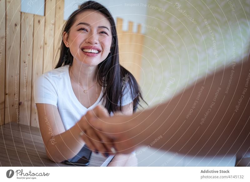 Glückliche asiatische Frau, die ihren Partner im Cafe begrüßt Termin & Datum Gruß Café Hände schütteln Lächeln Partnerschaft Paar Sitzung gestikulieren ethnisch