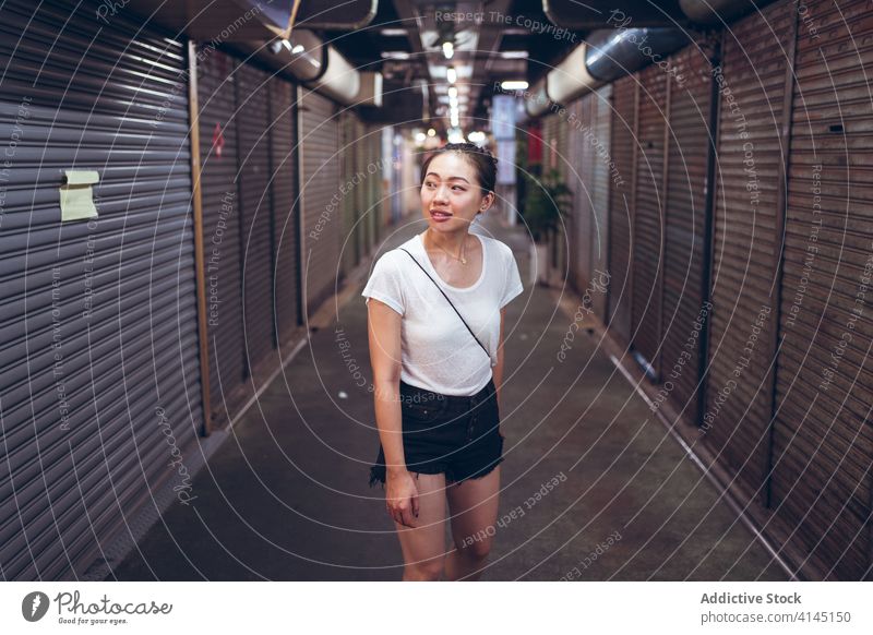 Junge ethnische Frau steht in einem unterirdischen Korridor Durchgang schließen Fensterladen urban Werkstatt Gewerbe ankündigen lesen jung asiatisch Lifestyle