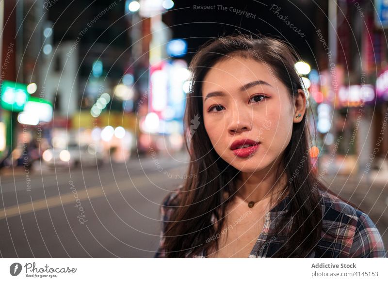 Positive ethnische Frau, die nachts auf einer Straße in der Stadt spazieren geht Großstadt Nacht Glück Lächeln heiter jung modern urban durchkreuzen