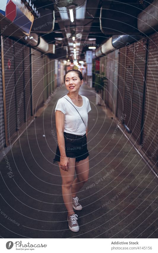Junge ethnische Frau steht in einem unterirdischen Korridor Durchgang schließen Fensterladen urban Werkstatt Gewerbe ankündigen lesen jung asiatisch Lifestyle