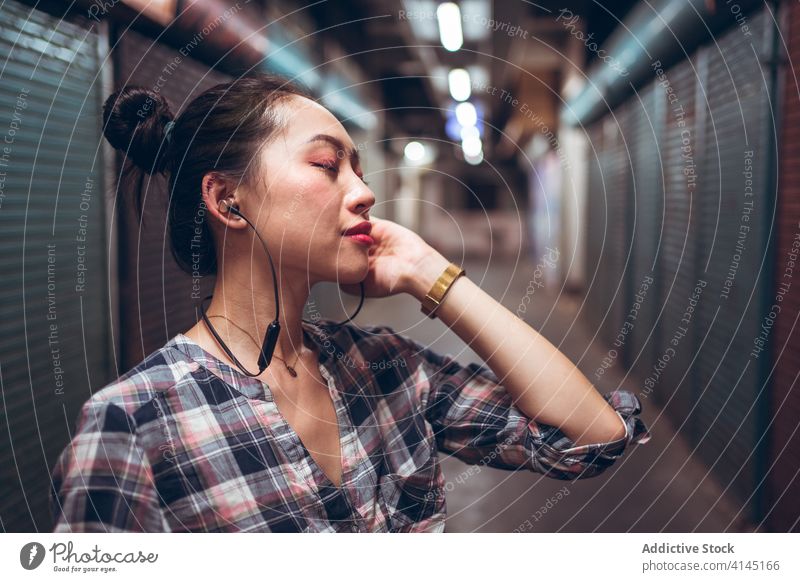 Frau mit Headset steht in einem unterirdischen Korridor Kommunizieren reden lässig urban asiatisch ethnisch tausendjährig Freude Gespräch Lifestyle modern