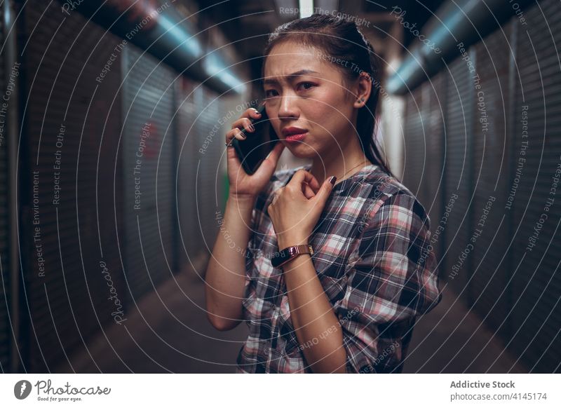 Besorgte junge Frau, die in einem unterirdischen Korridor mit ihrem Smartphone spricht Anruf Telefon erschrecken beunruhigt unglücklich Durchgang Stirnrunzeln