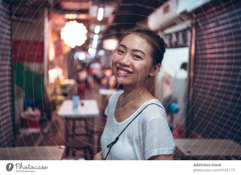 Positive asiatische Frau im Café stehend Glück Lächeln Straße Großstadt Nacht jung positiv heiter urban froh Freude ethnisch lässig Lifestyle leuchten Abend