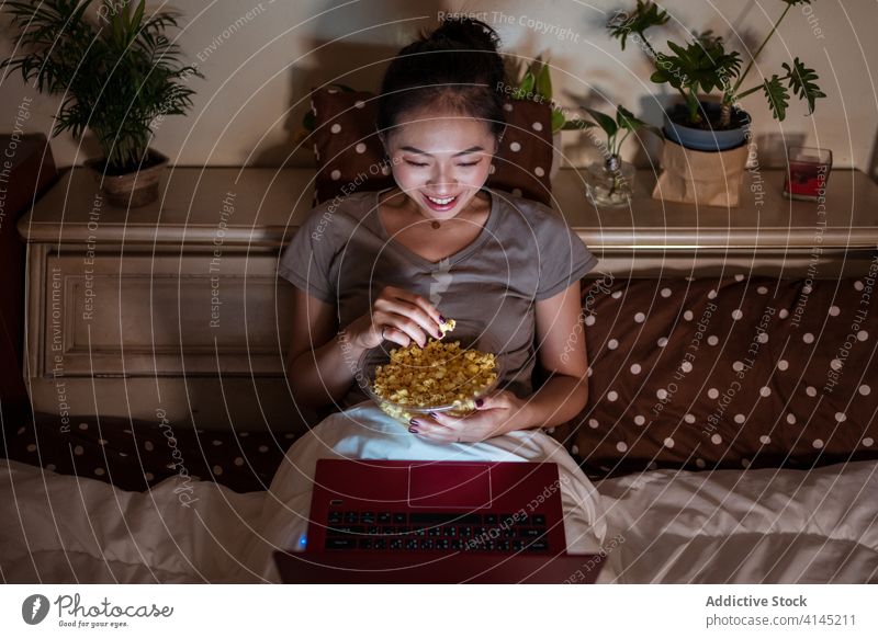 Inhalt Asiatische Dame sieht sich einen Film auf dem Laptop an und isst Popcorn Frau zuschauend Popkorn genießen essen sich[Akk] entspannen heimisch benutzend