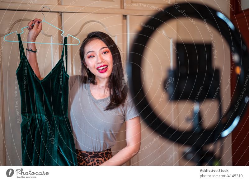 Stilvolle ethnische Frau nimmt Mode-Video-Blog auf vlog Aufzeichnen Outfit Kleid Blogger Influencer manifestieren jung asiatisch heimwärts Fotokamera Stativ