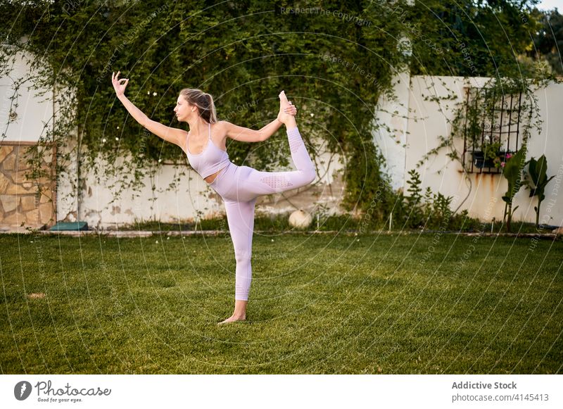 Anmutige Frau beim Yoga in Lord of the Dance-Pose Herr der Tanzpose Natarajasana beweglich Sportbekleidung Rasen Park ruhig Mudra gestikulieren grün Gesundheit