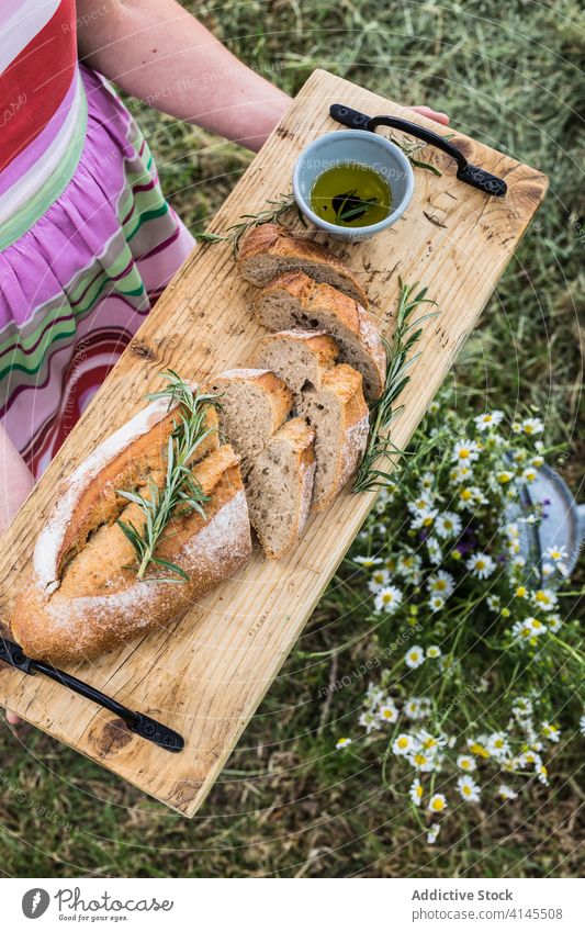 Anonyme Frau serviert appetitliches Brot mit Rosmarinzweigen im Freien dienen Schneidebrett weich oliv Erdöl selbstgemacht Gesundheit organisch frisch Kraut