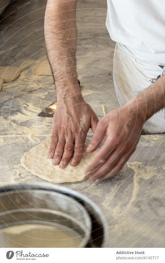 Pizzaiolo formt Pizzateig in der Küche zu einem Kreis Küchenchef Teigwaren Formular kreisen rund Koch vorbereiten kneten männlich Prozess kulinarisch
