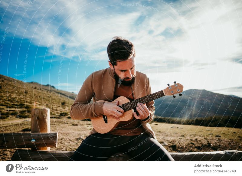 Bärtiger Mann spielt Ukulele auf dem Lande spielen Landschaft Zaun Himmel wolkig Musik puerto de la morcuera Spanien männlich reisen ernst Urlaub Ausflug Natur