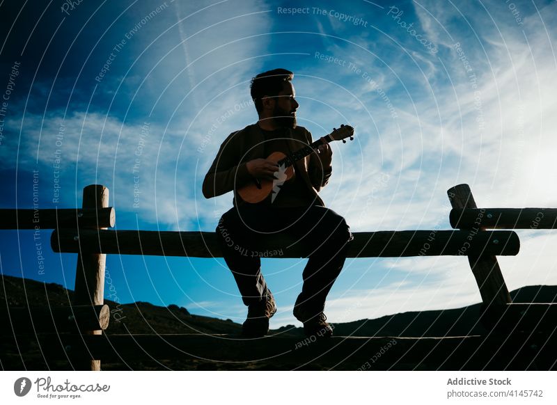 Bärtiger Mann spielt Ukulele auf dem Lande spielen Landschaft Zaun Himmel Silhouette wolkig Musik puerto de la morcuera Spanien männlich reisen ernst Urlaub