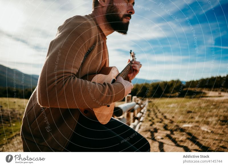 Anonymer bärtiger Mann spielt Ukulele auf dem Lande spielen Landschaft Zaun Himmel wolkig Musik puerto de la morcuera Spanien männlich reisen Urlaub Ausflug