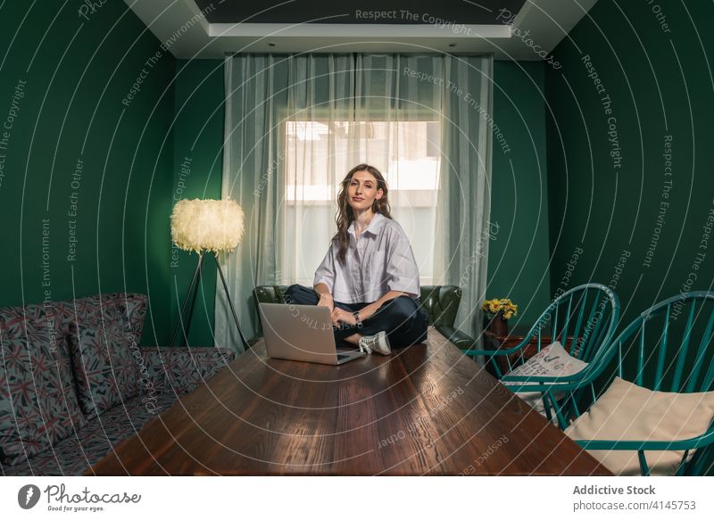 Junge Frau mit Laptop auf einem Tisch sitzend benutzend kreativ Browsen jung modern positiv heimwärts Appartement Design gemütlich Gerät Apparatur freiberuflich